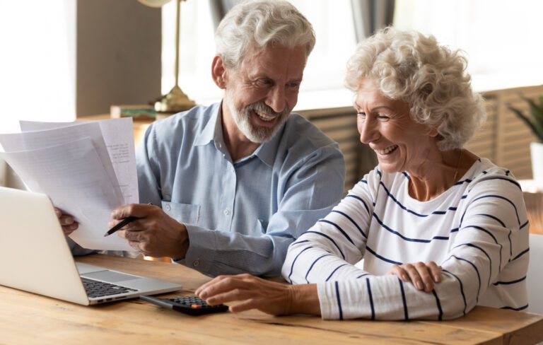 Happy senior couple looking at financial paperwork with a laptop and calculator