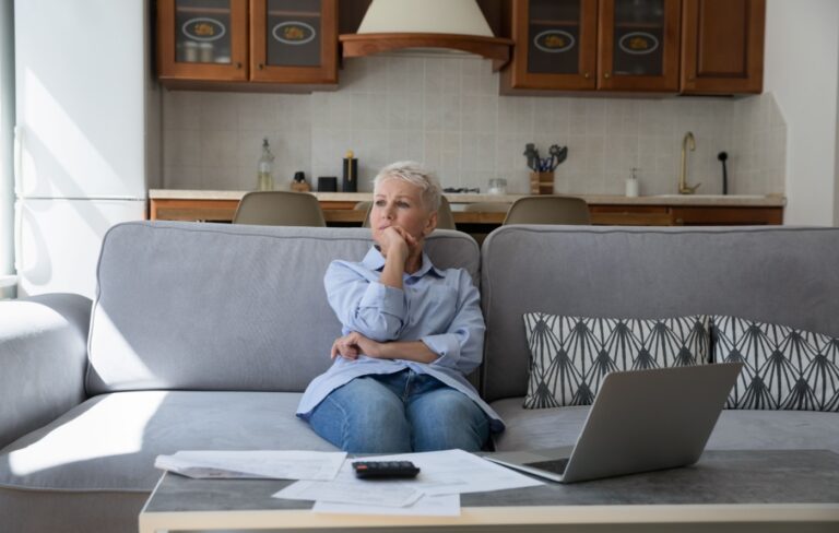 Thoughtful senior woman with a calculator, laptop and paperwork