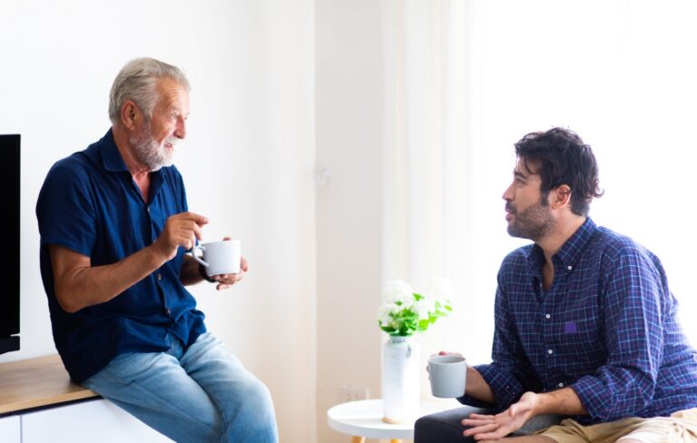 Father and adult son talking over cups of coffee