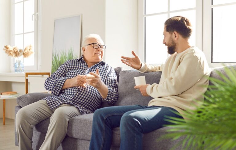 A senior man sitting talking to his adult son on a sofa