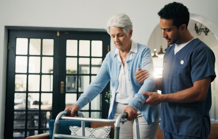 A carer helping a senior woman walk with a frame