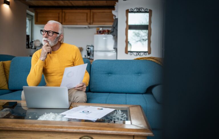 Thoughtful senior man using a laptop and holding financial paperwork