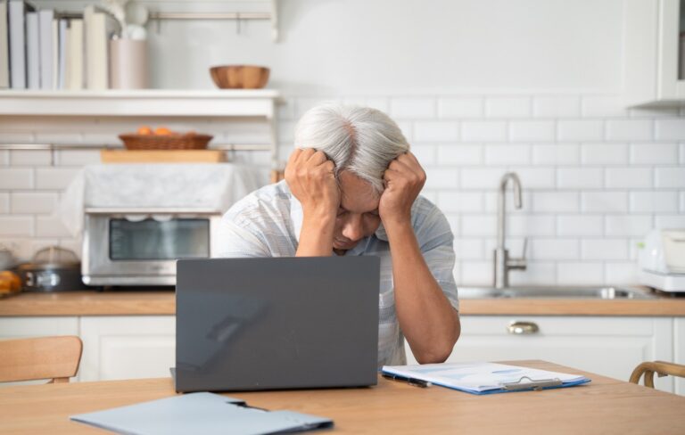 Senior man sitting in front of a laptop with his head in his hands