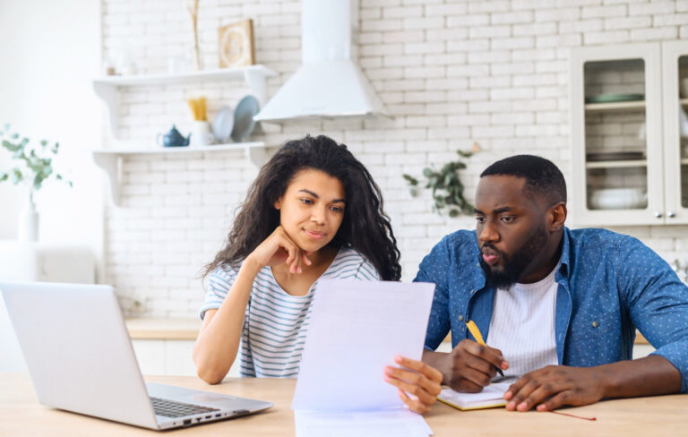 A multiracial couple sitting in front of a laptop looking at paperwork